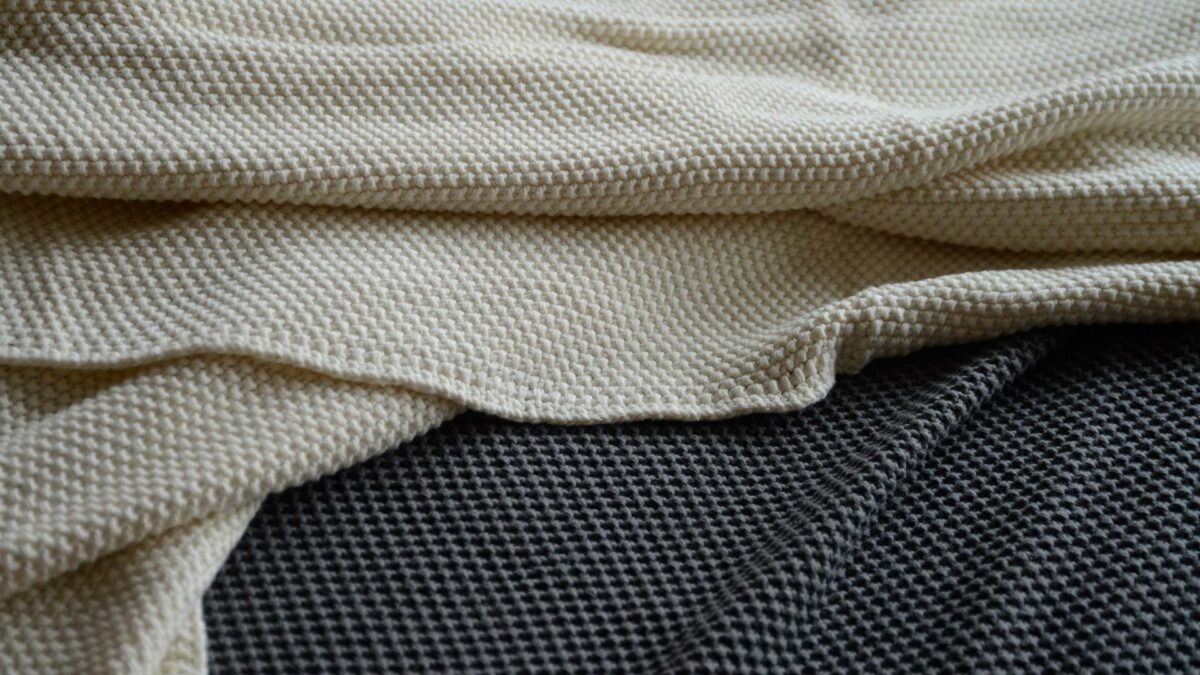 moss stitch knitted cotton throws in cream, and grey shown close up