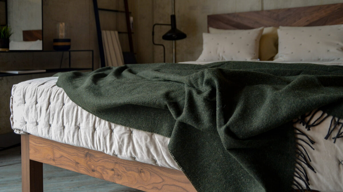 reversible pure wool throw in Fir Green shown draped on a bed