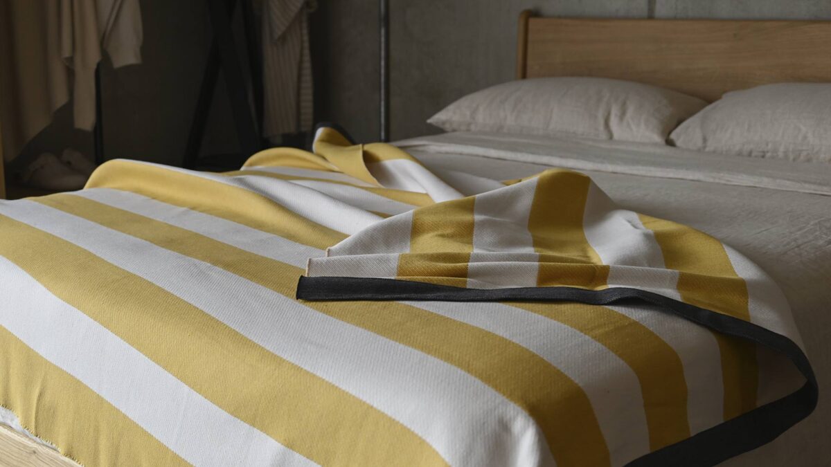 Deep yellow and ivory striped throw with green edge laid over a stone linen duvet cover.