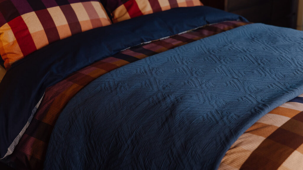 blue diamond textured bedspread on top of check patterned bedding.