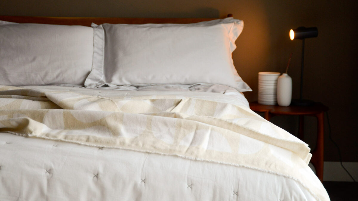 graphic patterned soft cotton throws in ivory and ecru, shown on a bed