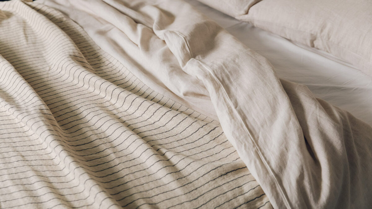 close up of relaxed look luxury linen bedding in Ecru shown with a striped cotton throw