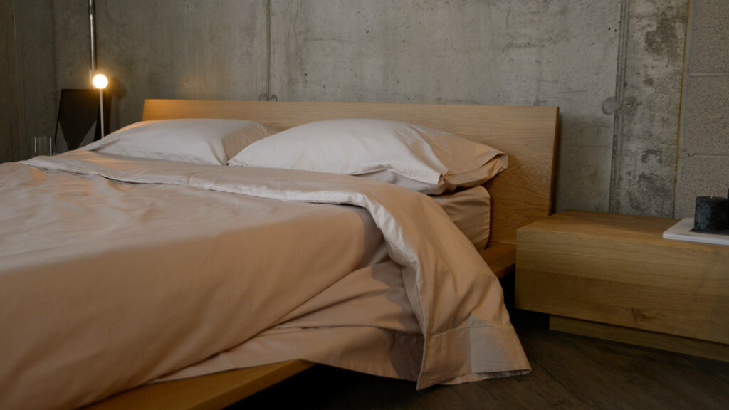 soft sheen Egyptian cotton bedding in shell colour shown on a low bed