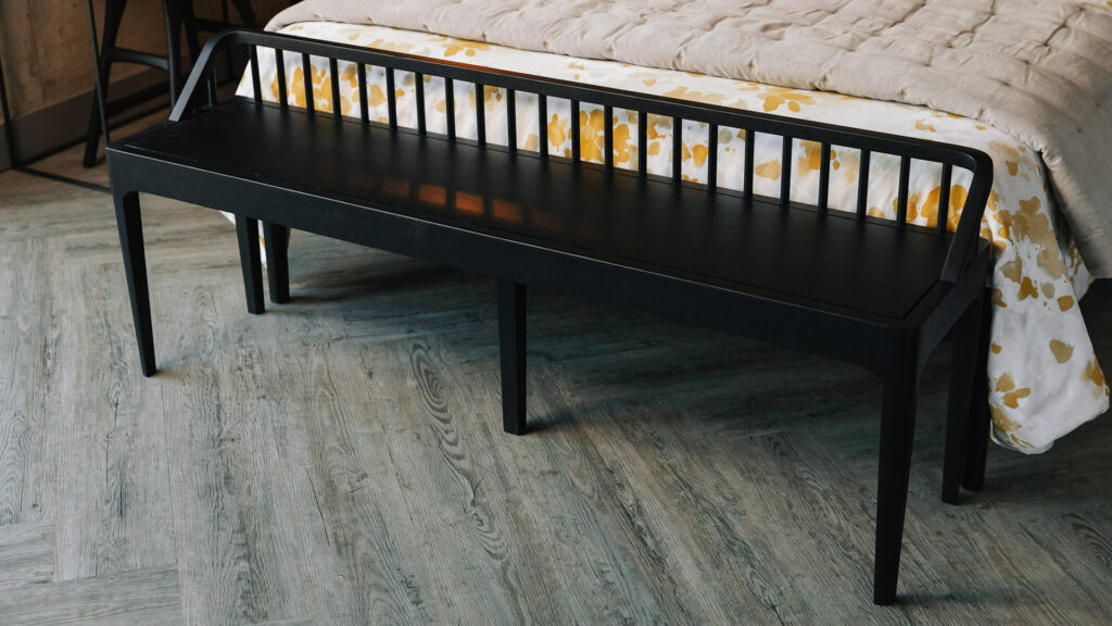 slender spindle bench in black oak shown at the end of a kingsize bed