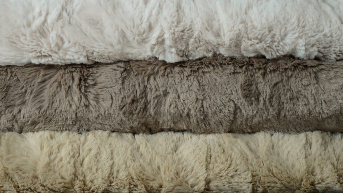 softest faux fur throws in a range of neutral grey and stone colours shown in a stack