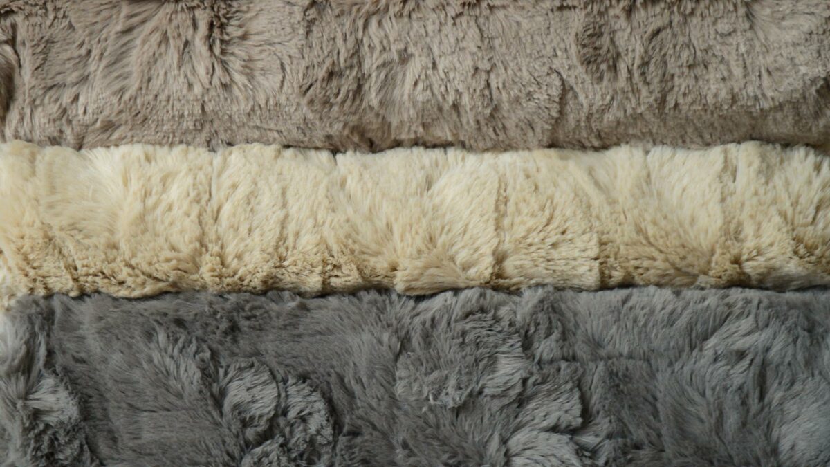 softest faux fur throws in a range of neutral grey and stone colours shown in a stack