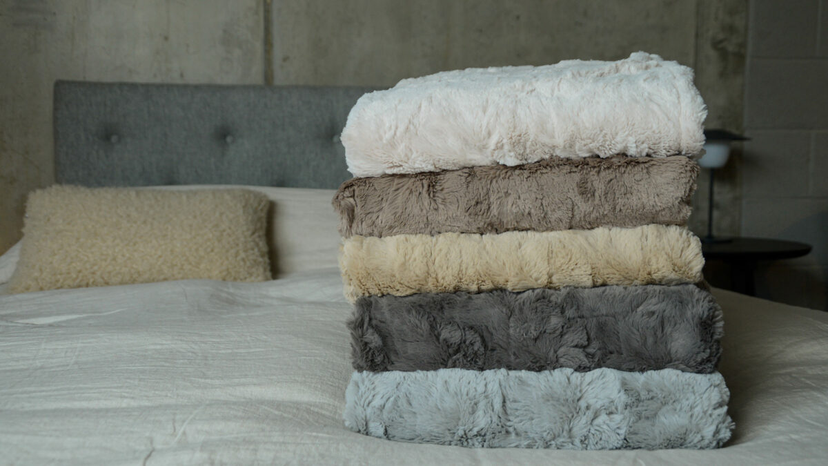 softest faux fur throws in a range of neutral colours shown in a stack