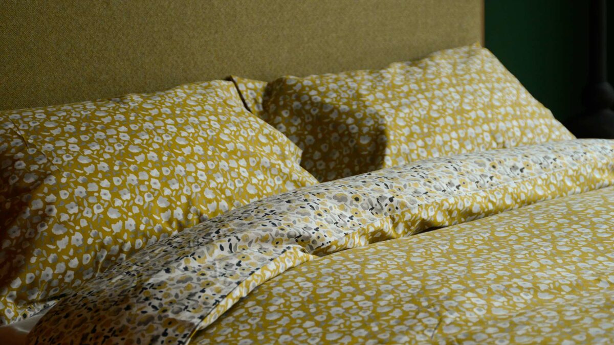 modern blossom patterned reversible duvet cover set in yellow, white and grey shown on a bed