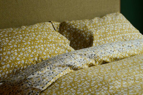 modern blossom patterned reversible duvet cover set in yellow, white and grey shown on a bed