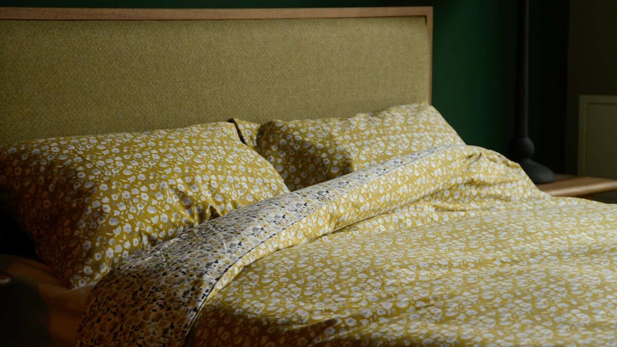 modern floral patterned reversible duvet cover set in yellow ochre and grey shown on a bed