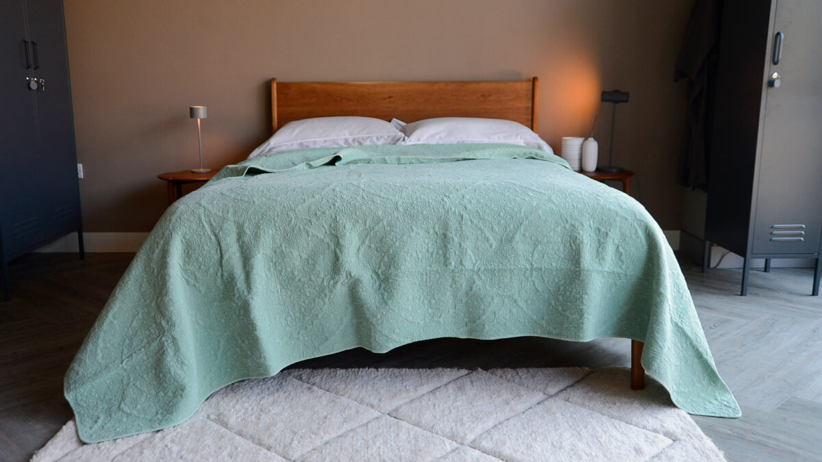 floral embroidered quilted bedspread in sage green shown on a kingsize bed