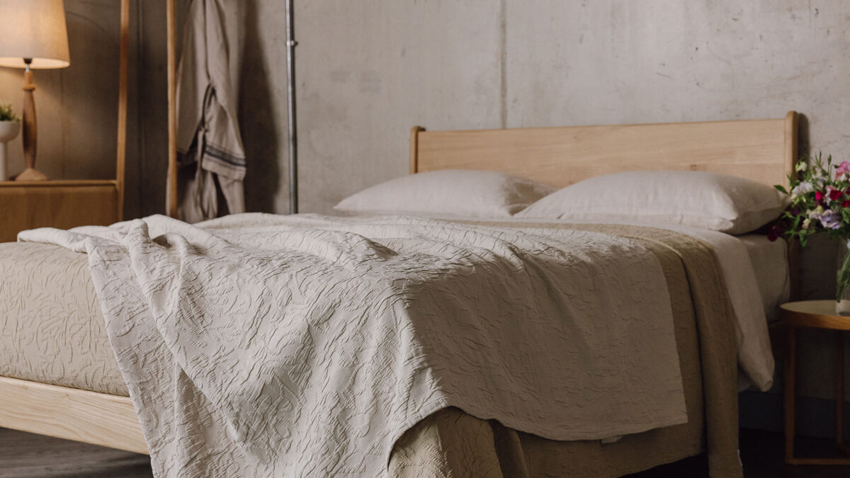 Floral textured cotton bedspreads in the colours ecru and sand on top of the English oak Camden bed base.