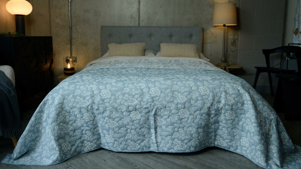 Powder blue and ivory floral patterned reversible quilted bedspread shown on a kingsize bed