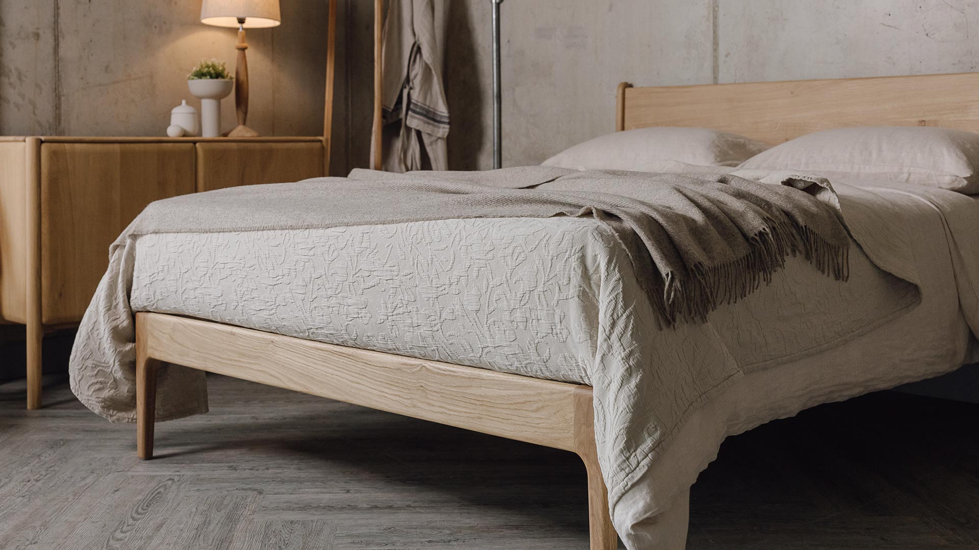 3/4 angle photo of an oak bed with stone linen and a greige lambswool throw.