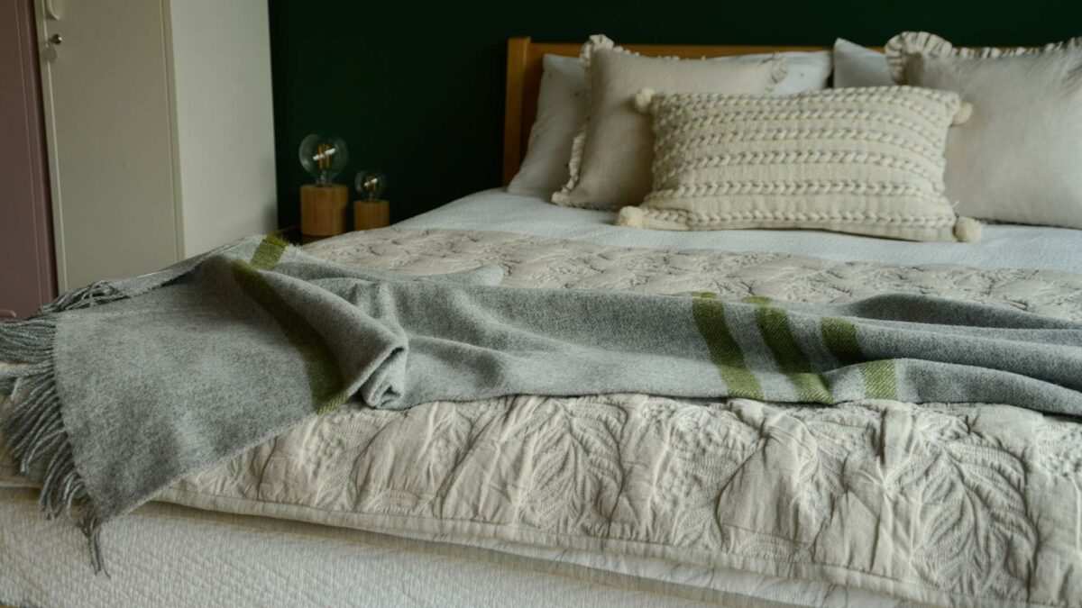 grey marl woollen throw with green stripes shown on a bed