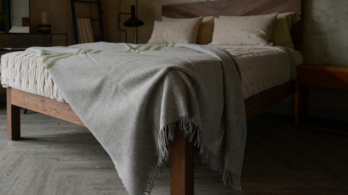 grey marl woollen throw with green stripes shown on a bed