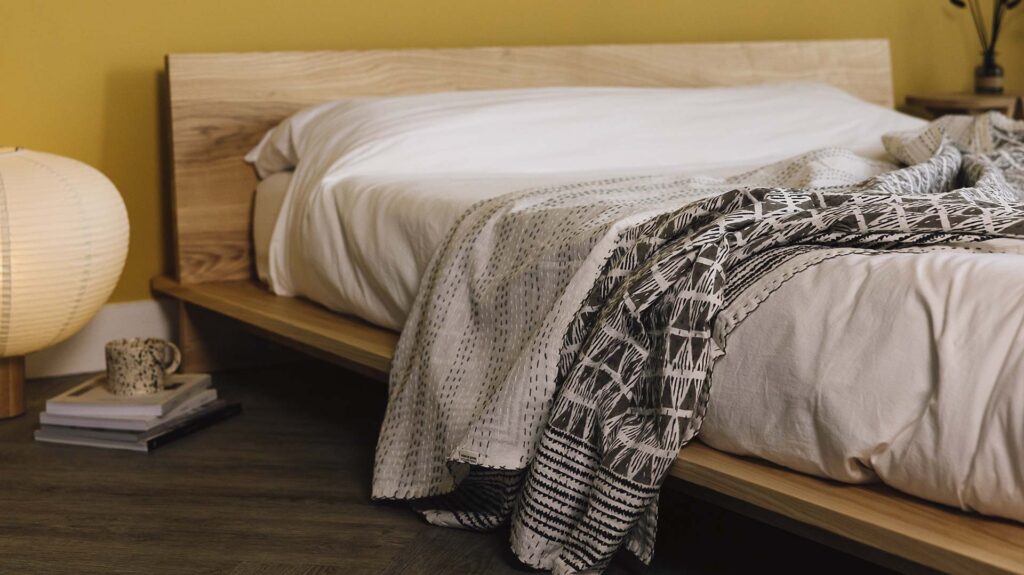 Reversible kantha bedspread with grey block print in a triangle design draped over an ash bed with white bed linen.