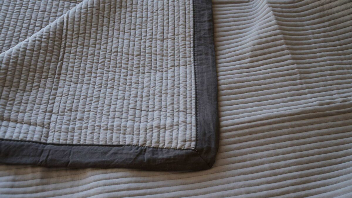 stitched stripe quilted bedspread in silver grey with a dark grey border shown close up