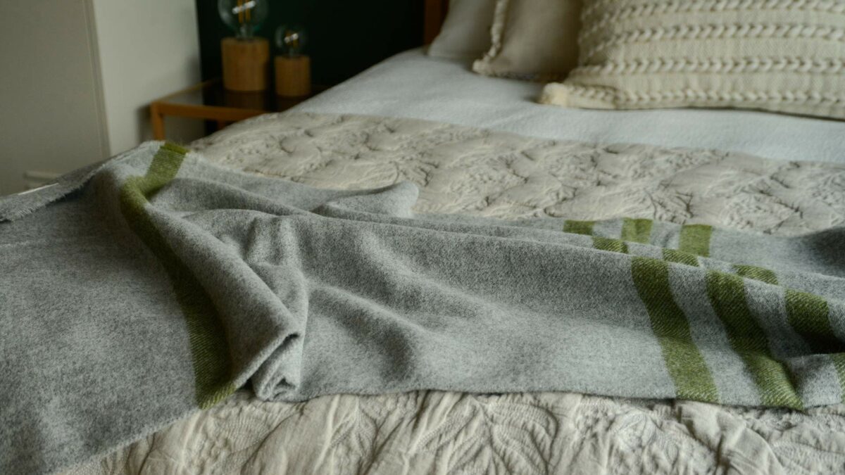 grey marl woollen throw with green stripes shown on a bed