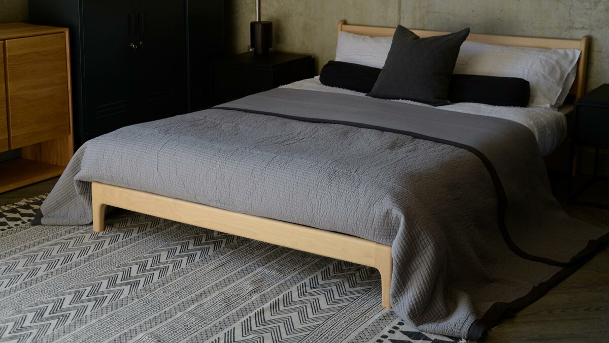 plain grey large quilted bedspread shown on a low wooden bed