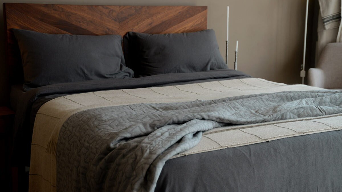 Grey textured pattern bedspread made from recycled cotton shown draped on a kingsize bed