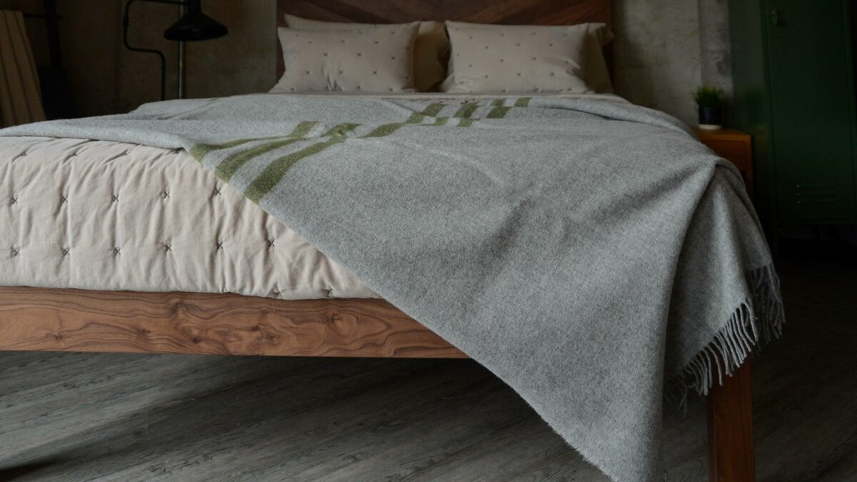 grey marl woollen throw with green stripes shown on a bed