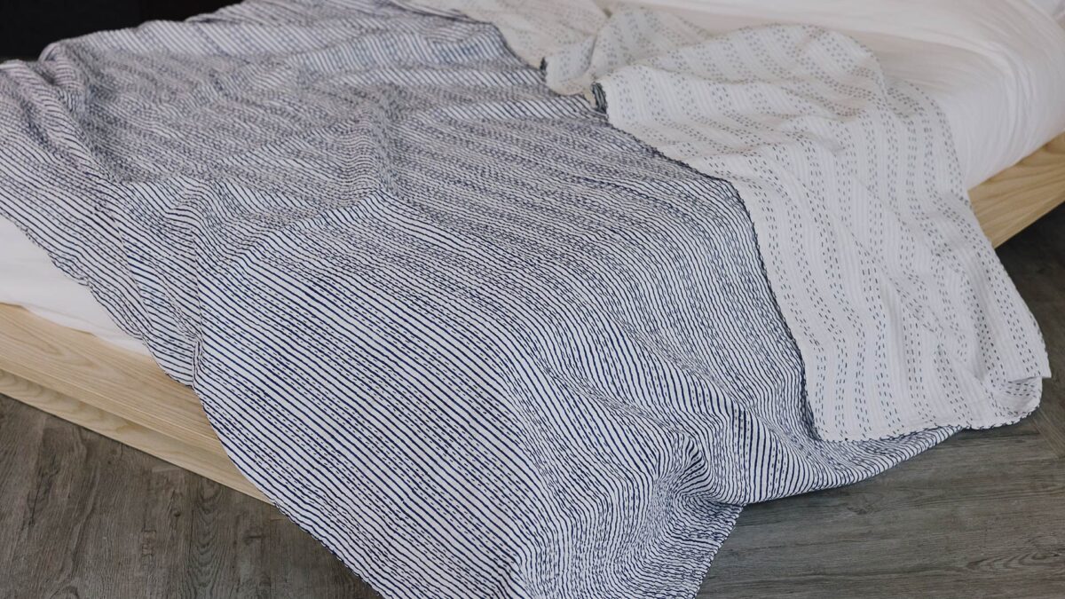 Blue and white striped handmade kantha bedspread draped across the top of a low bed.