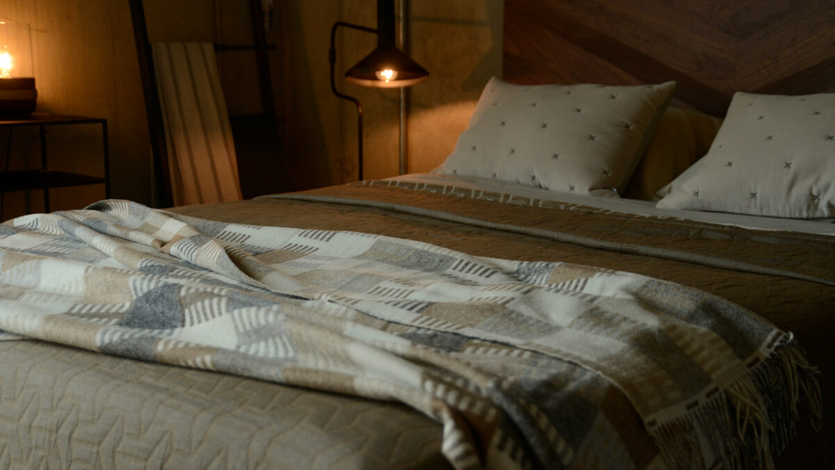 patterned Merino wool throw in neutral colours shown on a bed