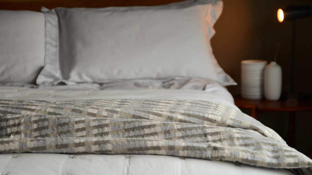 patterened stripey fluffy throw in ivory and taupe tones shown on a bed