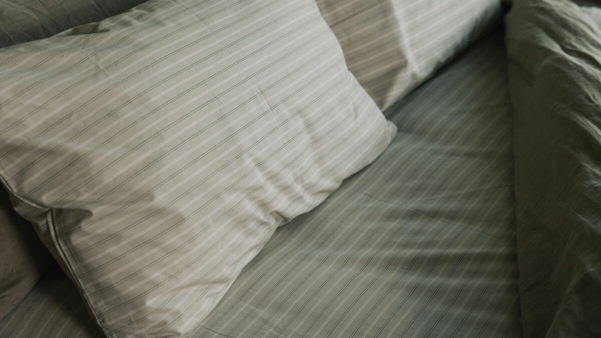 sage green striped fitted sheet and pillowcase set shown on a bed