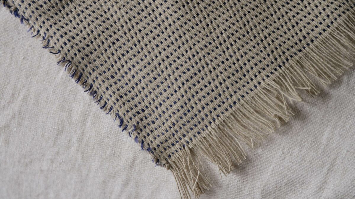 a close up of the woven linen bedspread in beige and with purple threads