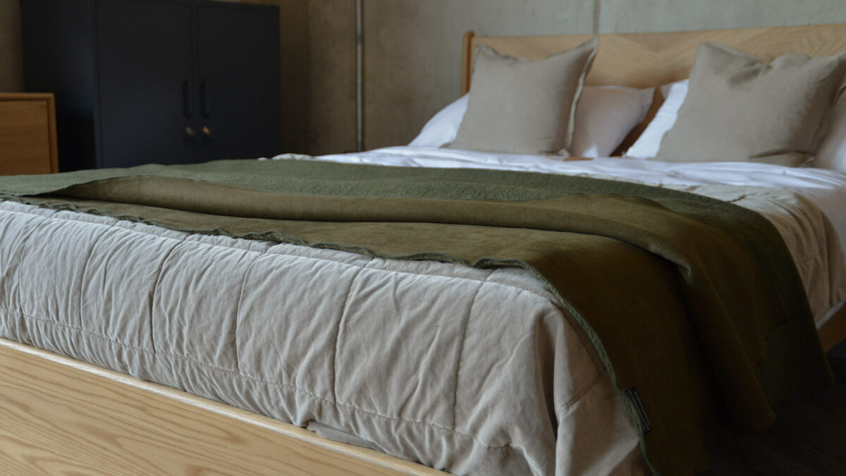 faux sheepskin throw in olive green shown on the end of a bed