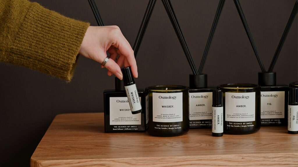 Close up image of a hand holding an Aery roll-on perfume oil. Behind this, there is a row of Aery candles, roll-on oils and diffusers.