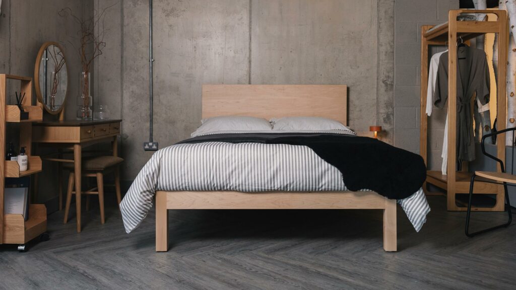maple Bamford bed with grey striped bedding and black sheepskin