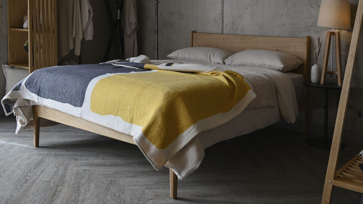 modern abstract design throw with grey and yellow blocks draped across a bed with stone bedding.