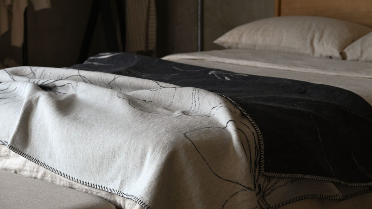 reversible throw in charcoal and ivory. Floral pattern. Neatly spread across a made bed.