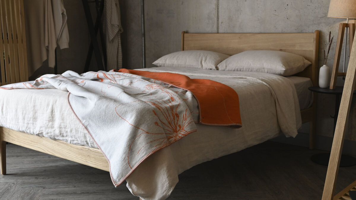 Oak bed with neutral linen and an orange and ivory floral patterned throw on the top.