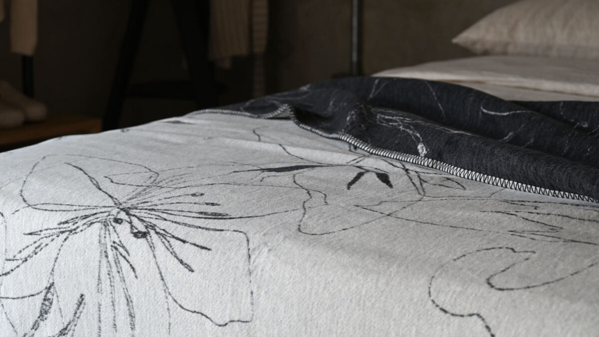 Charcoal and ivory throw with large floral pattern draped over the top of a made bed.