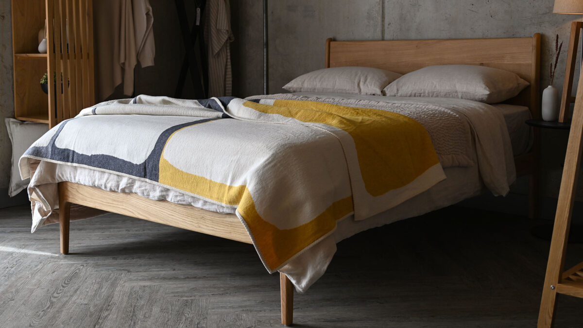throw with yellow, Ivory and charcoal abstract blocks photographed draped across the foot end of a made bed.
