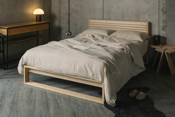 A special edition Leith bed in Ash wood with walnut stripes to the headboard panel shown with stone coloured bedding