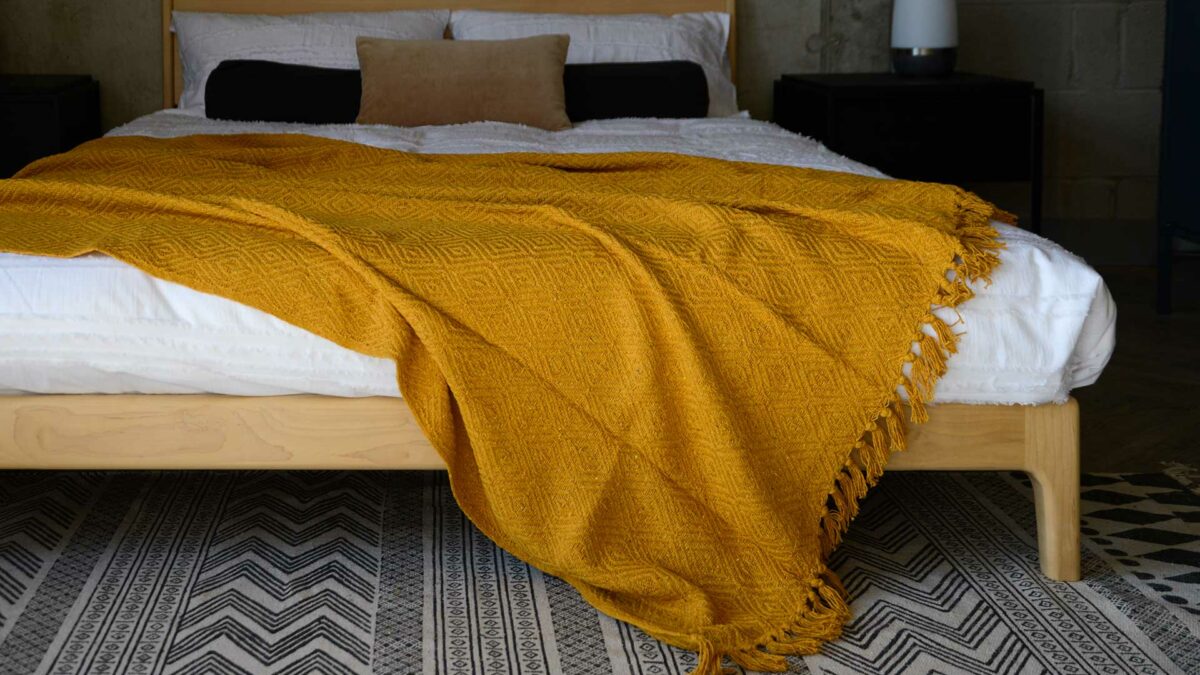 mustard yellow diamond weave throw shown on a kingsize wooden bed