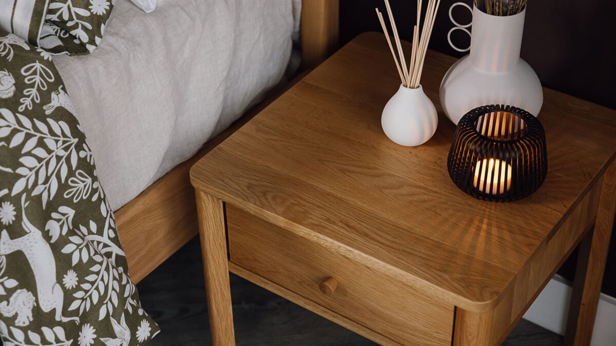 Close up of an oak bedside table with drawer. Vase, diffuser and candle holder on the top.