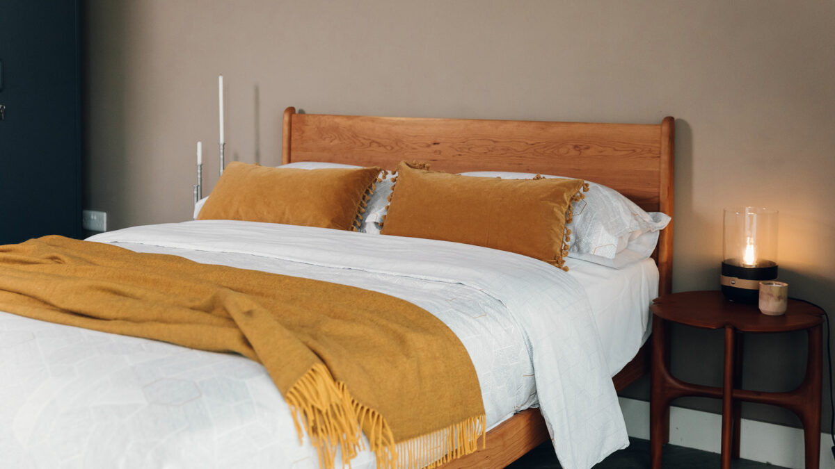 yellow ochre reversible woollen throw shown on a kingsize wooden bed