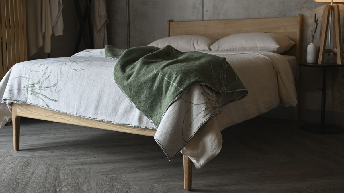 reversible throw in olive and ivory. Floral pattern. Neatly spread across a made bed.