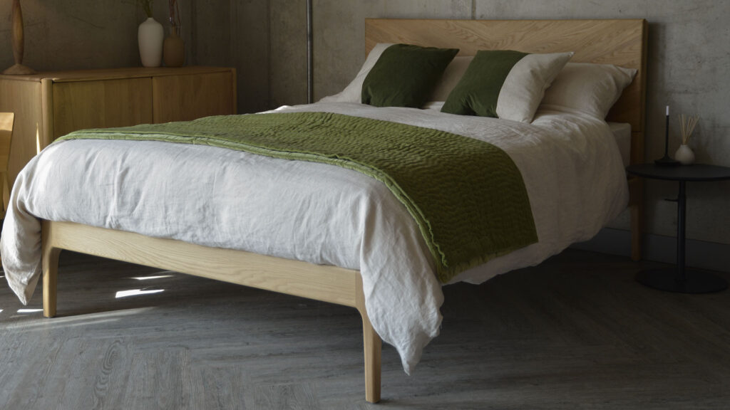 oak bed dressed in beige linen, a green throw and green and ecru cushions.