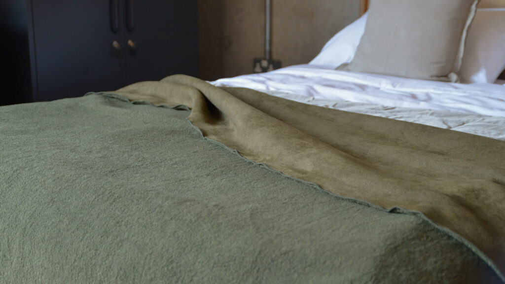 faux sheepskin blanket in olive green shown on the end of a bed