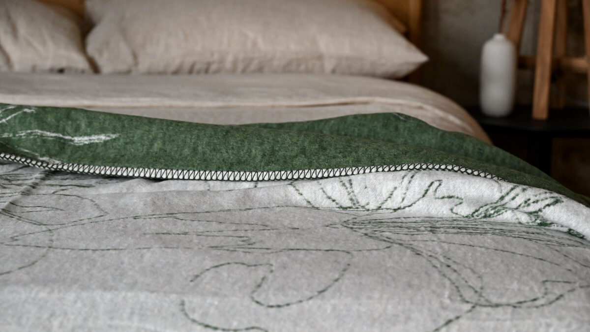 closeup of a reversible throw in olive and ivory. Floral pattern. Neatly spread across a made bed.
