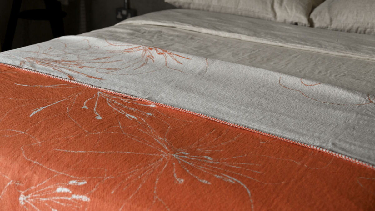 reversible throw in orange and ivory. Floral pattern. Neatly spread across a made bed.