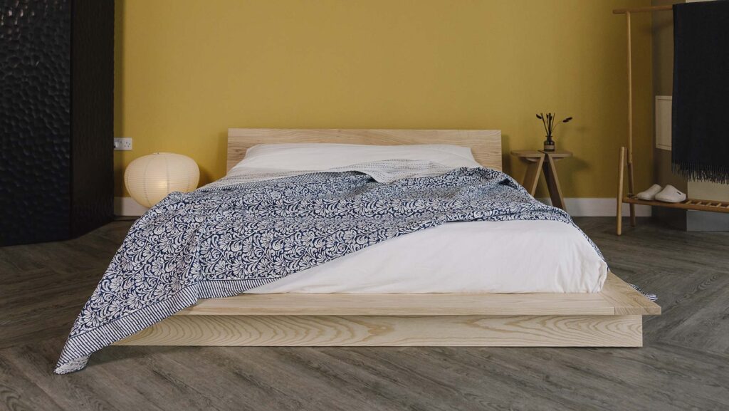 Ash platform bed frame with white bedding and a blue floral bedspread.