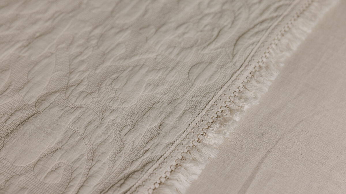 Close up of the stone coloured textured floral cotton throw's fringe detail.